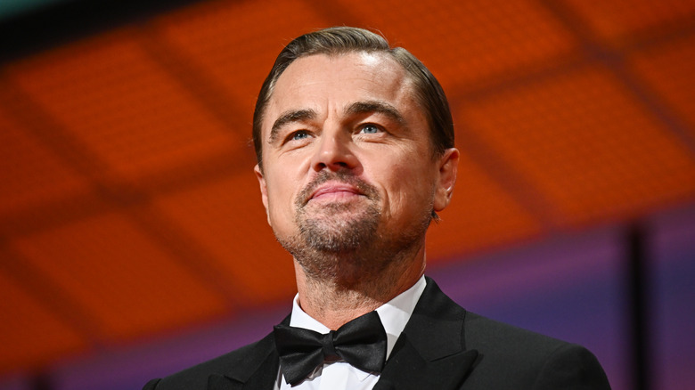 A split image of Lauren Sanchez looking at the camera while wearing an off-shoulder dress and bold makeup, and Leonardo DiCaprio sporting a Tuxedo as he smiles gently.