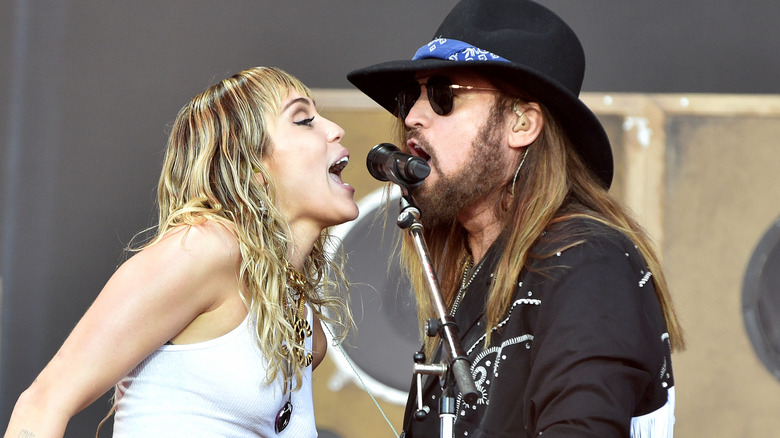 Miley and Billy Ray Cyrus signing with the same microphone on stage