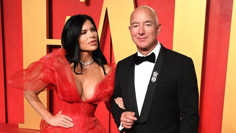 Lauren Sánchez clings to the arm of Jeff Bezos, who's focused on the camera.