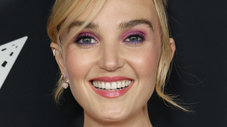 Chloe Fineman smiles in a red and pink gown