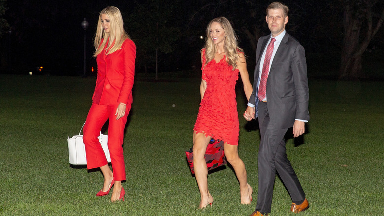 Ivanka Trump wearing red pantsuit and walking across White House lawn with Lara and Eric Trump