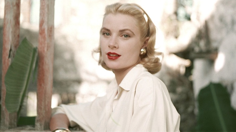 Grace Kelly posing for a photograph outdoors in 1955 with red lipstick and gold accessories