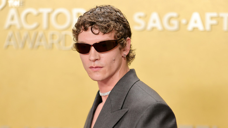 Connor Storrie wearing sunglasses and a grey suit jacket and silver necklace