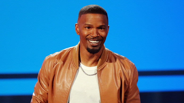 smiling Jamie Foxx posing in white shirt and tan jacket