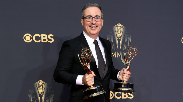 John Oliver smiling and holding two Emmys