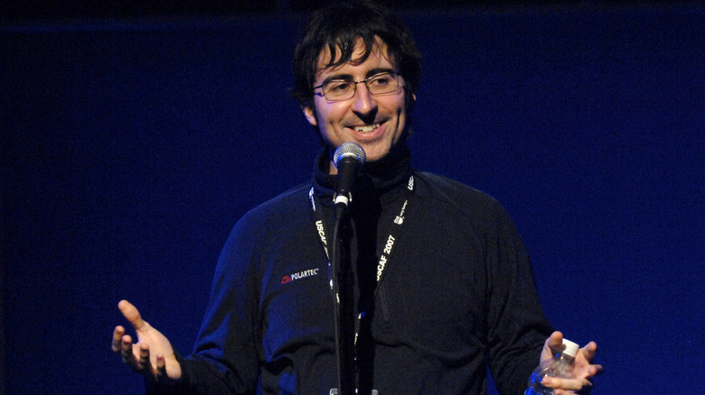 John Oliver smiling on stage with a microphone