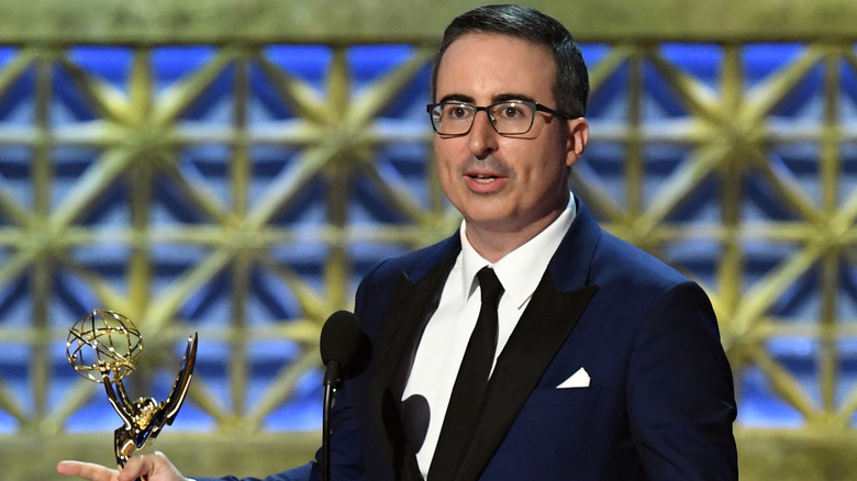 John Oliver speaking at podium and holding an Emmy