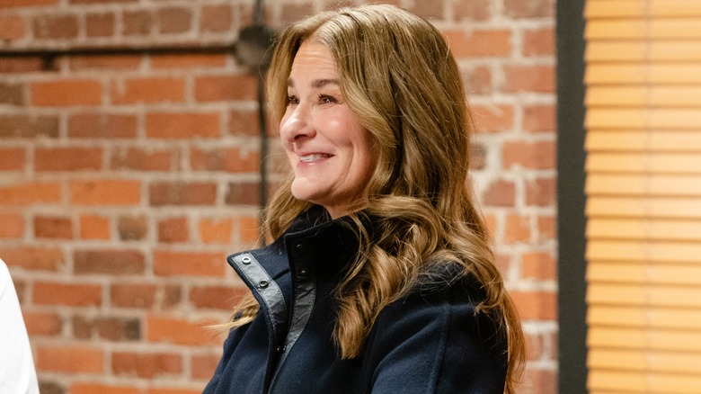 Melinda Gates, dressed in a black outfit, flashes a wide smile.