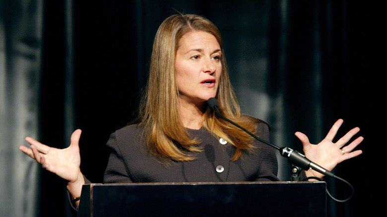 Melinda Gates speaks into a microphone as she gestures with her hands.