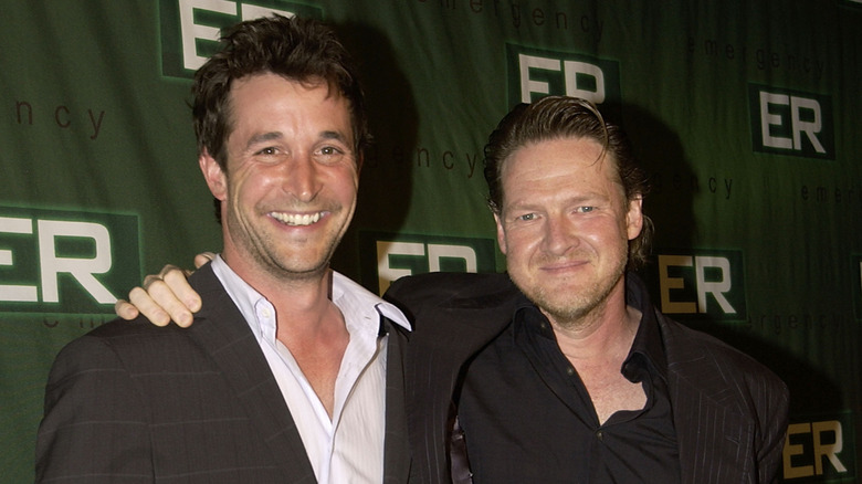 Noah Wyle in a grey suit jacket and Donal Logue in a black striped suit jacket in front of a step and repeat for ER