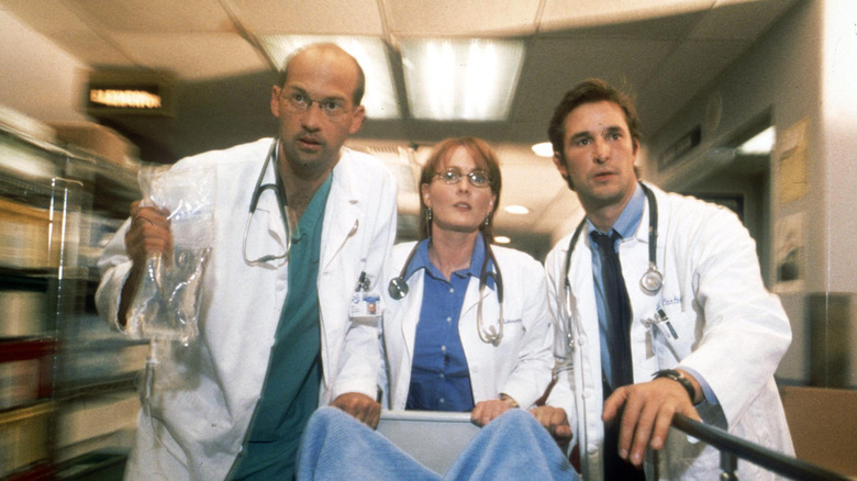 Noah Wyle on set of ER wearing a lab coat and stethoscope with his co-stars