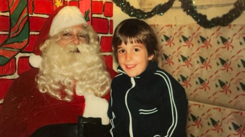 A young Noah Wyle wearing a black striped jacket while sitting on Santa's lap