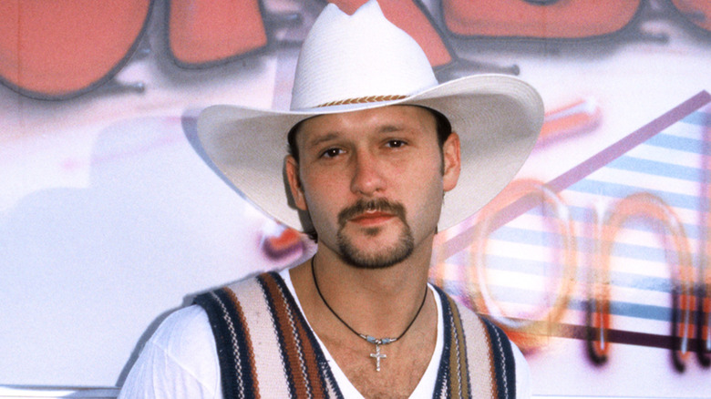Tim McGraw posing in front of a sign, wearing a white cowboy hat