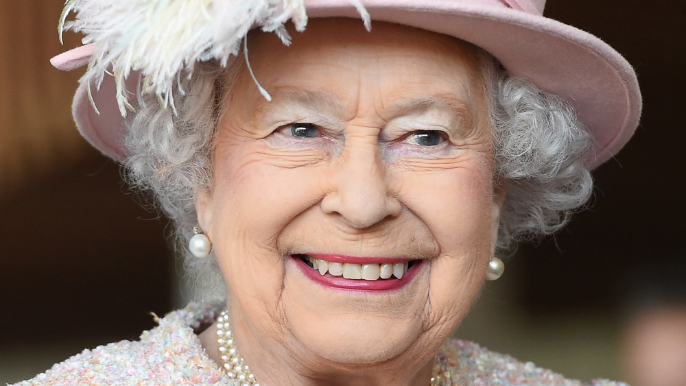 Queen Elizabeth II smiling at an event while wearing light pink