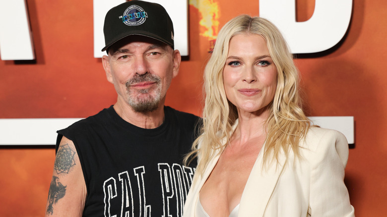 Billy Bob Thornton wearing a cut off t-shirt and black baseball cap with Ali Larter wearing a white blazer and white satin bra