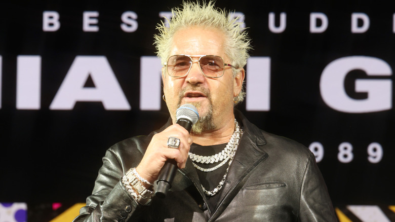 Guy Fieri on stage holding a microphone and an award