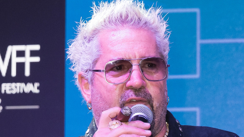 Guy Fieri on stage holding a microphone and cigar