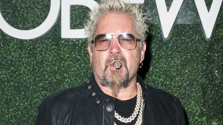 Guy Fieri on red carpet wearing leather jacket and smoking cigar