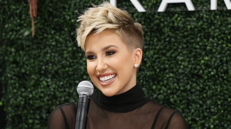 Wearing a spiky fade haircut, Savannah Chrisley Smiles in front of a microphone.