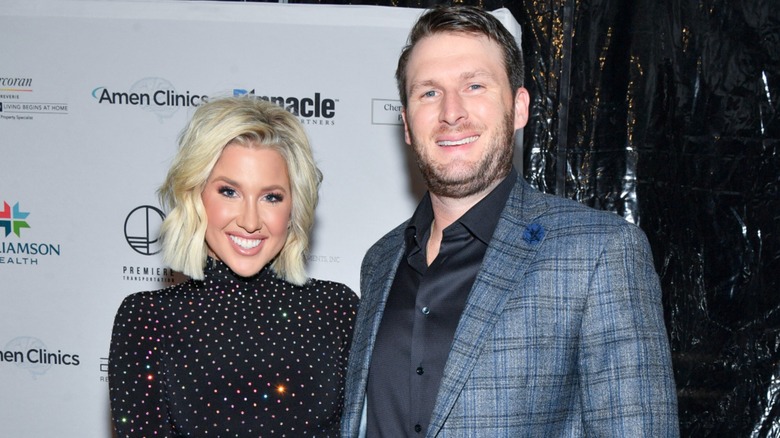Savannah Chrisley and Robert Shiver lean toward each other while all smiles on the red carpet