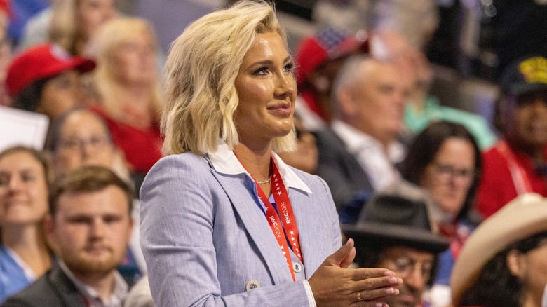 Savannah Chrisley looks up and presses her hands together against the background of a crowd during a political event.