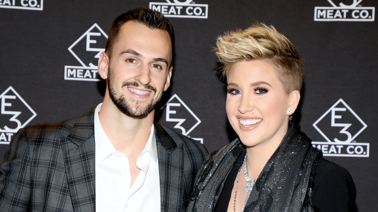Savannah Chrisley and Nic Kerdiles lean next to each other and wear wide smiles on the red carpet.