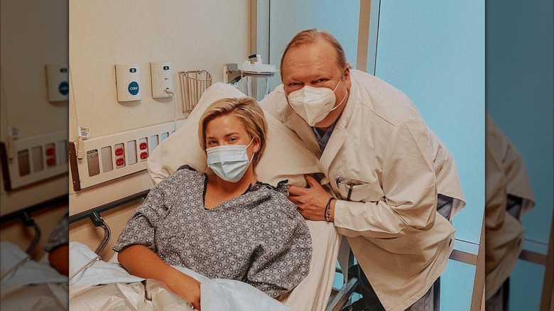 Savannah Chrisley wears a mask while leaning on an examination chair, as her masked doctor leans toward her.