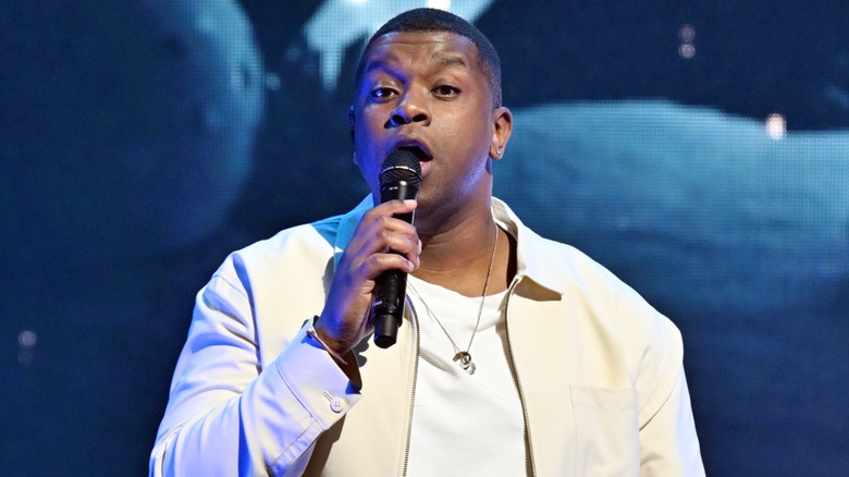 Dressed in a white-cream outfit, Matt Sallee sings into a microphone.