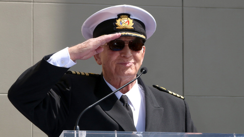 Gavin MacLeod wearing hat and sunglasses giving salute