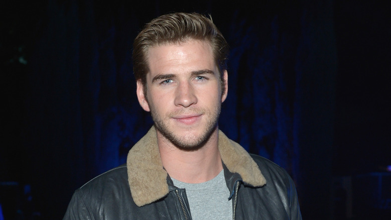 Liam Hemsworth smirking and wearing leather jacket