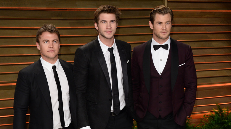 Luke, Liam and Chris Hemsworth posing in black suits