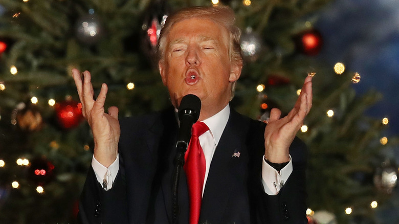 Donald Trump gestures animatedly on stage in front of a Christmas tree.