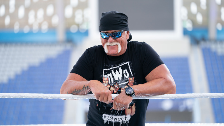 Hulk Hogan wearing a black t-shirt and leaning on the rope inside a wrestling ring