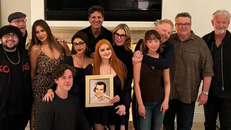The Modern Family cast posing with a framed photo of Ty Burrell