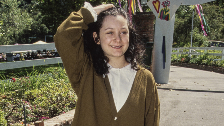 Sara Gilbert walking outdoors and smiling while running a hand through her hair in 1993