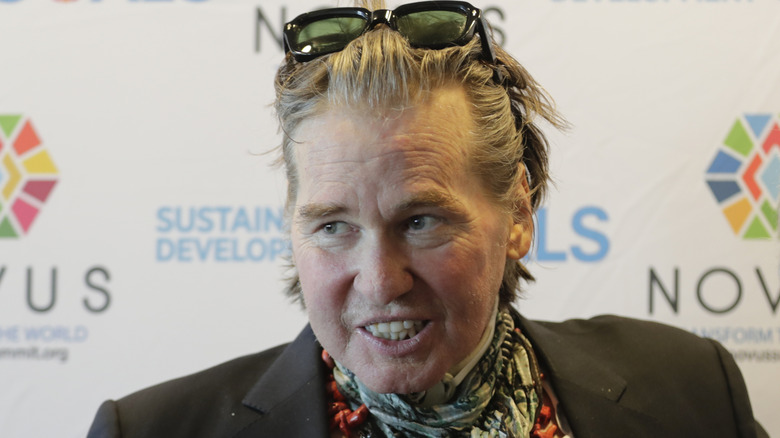 Val Kilmer wearing a colorful scarf to hide his breathing tube