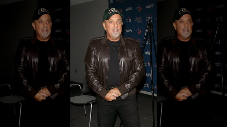 Billy Joel posing in a brown leather jacket and baseball cap