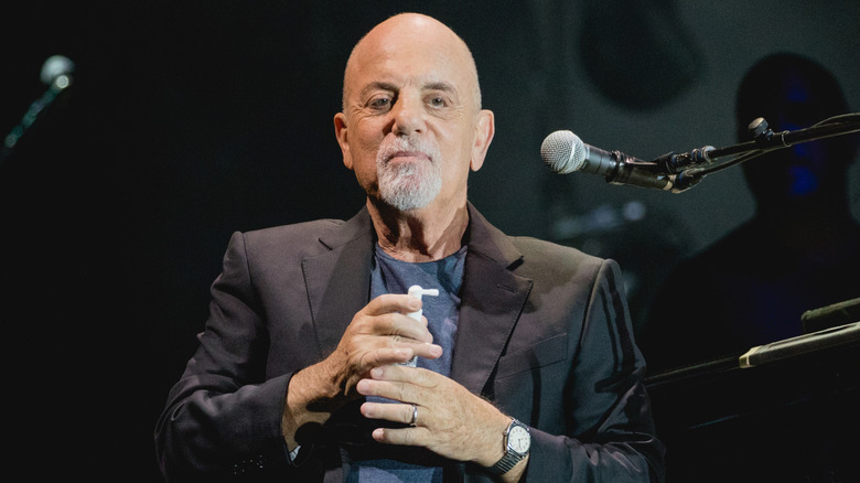 Billy Joel wearing a silver watch and holding a white spray bottle onstage