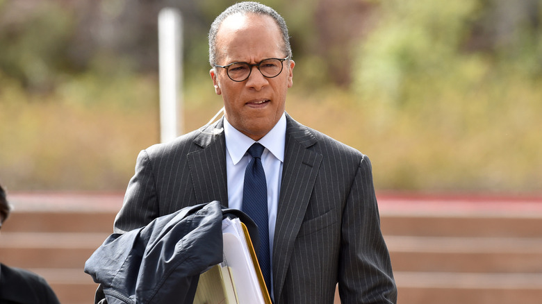 Lester Holt walking with a pile of documents.