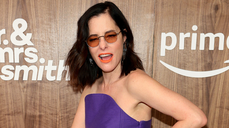 Parker Posey posing animatedly on a red carpet.
