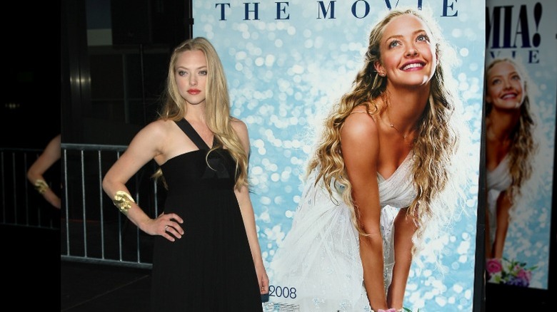 Amanda Seyfried standing with Mamma Mia poster