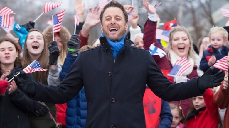 Chris Harrison with beard in front of Bachelor Winter Games fans with international flags