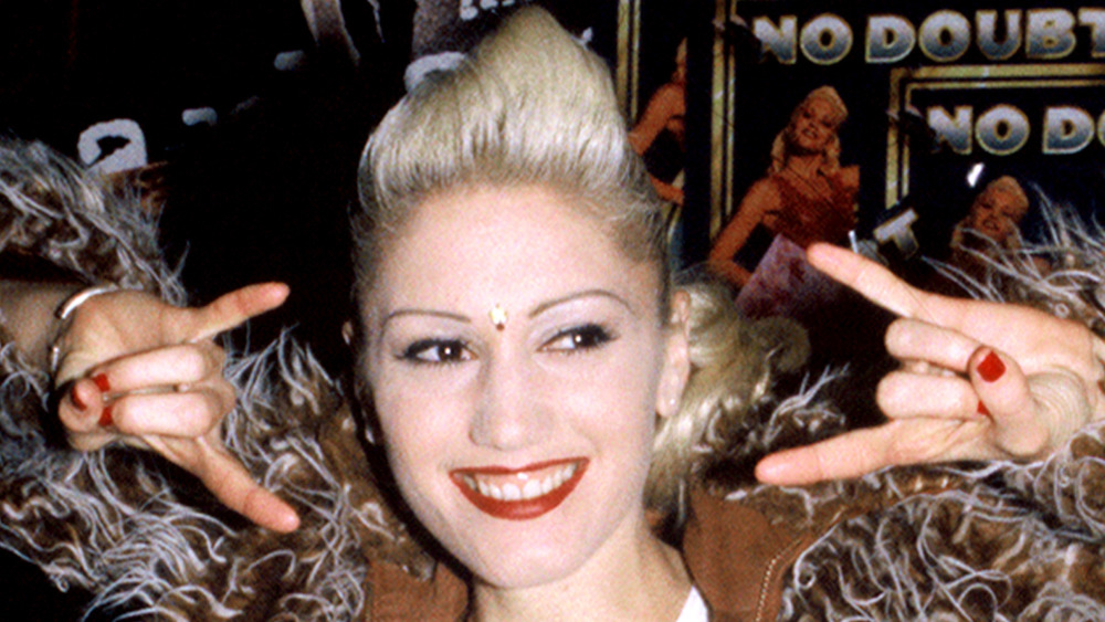 Gwen Stefani smiling while throwing up a rock on sign