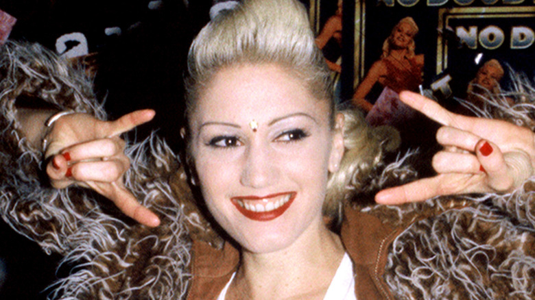 Gwen Stefani smiling while throwing up a rock on sign