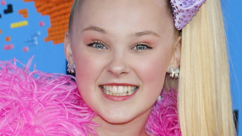 JoJo Siwa poses in a pink and purple outfit.