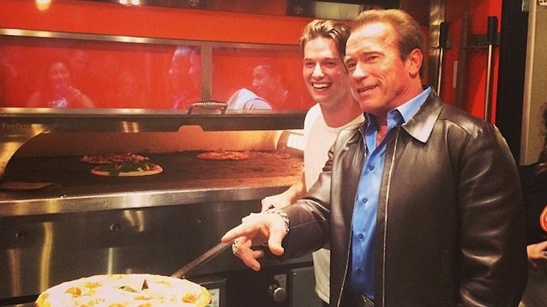 Patrick Schwarzenegger holding a pizza with father Arnold Schwarzenegger at his pizza restaurant