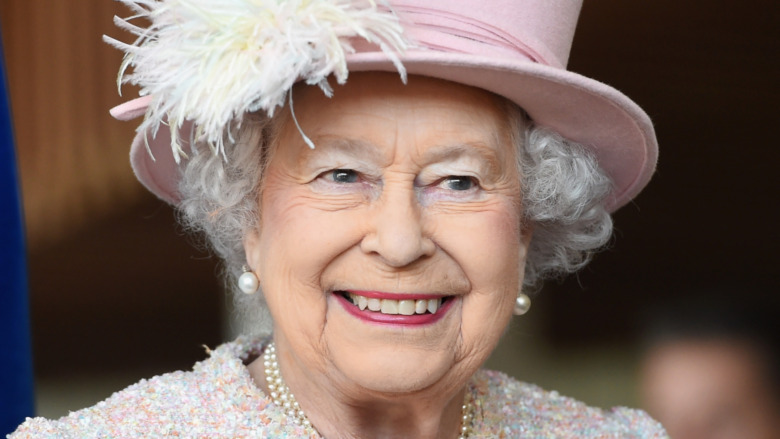 Queen Elizabeth smiles in pink hat.