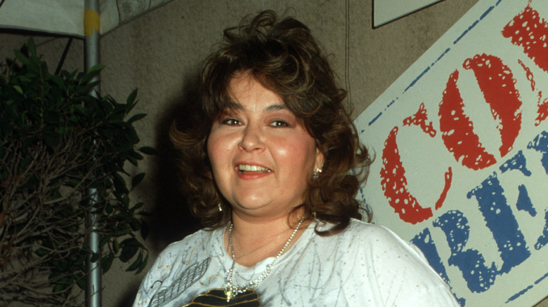 Roseanne Barr stands in front of a sign promoting HBO's "Comic Relief" in 1987