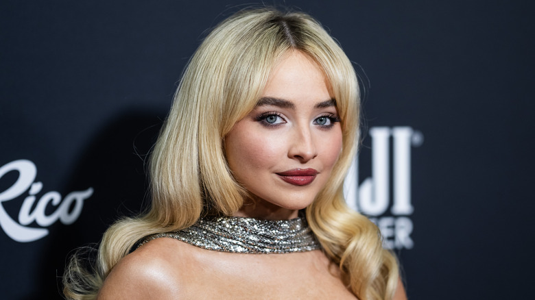 Sabrina Carpenter with long blonde hair wearing a silver sparkling scarf