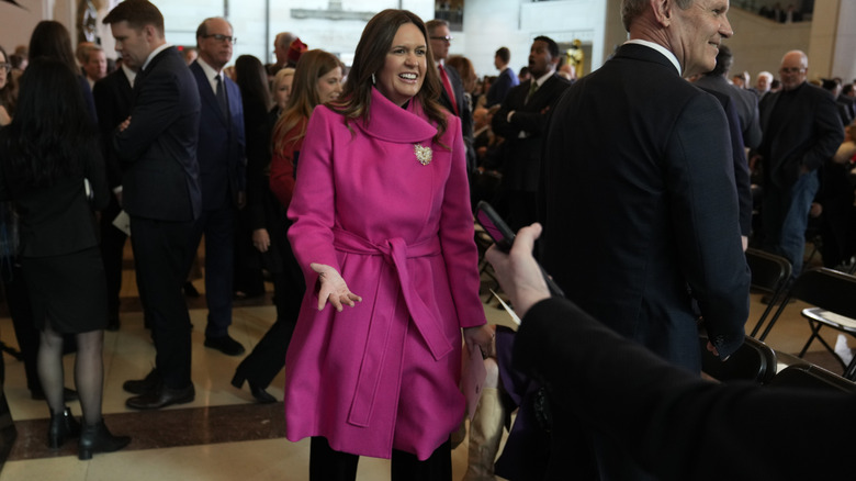 Sarah Huckabee Sanders walking into crowded room in pink coat